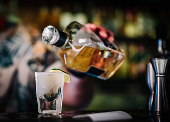 Bartender pouring strong alcoholic drink into shot glass in bar