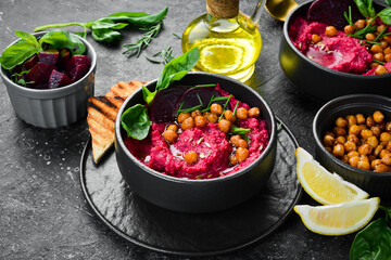 Healthy vegetarian food: Hummus. Beet and chickpea hummus in a bowl. On a concrete black background.