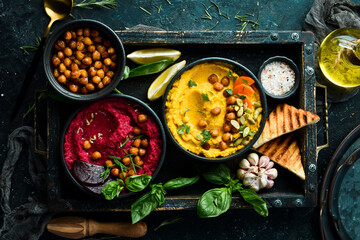 Colorful hummus bowls. Flat-lay of various vegetarian dips hummus. On a concrete black background.