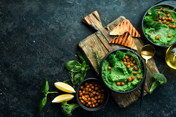 Green hummus. Hummus from chickpeas and spinach and broccoli, with olive oil and spices. Healthy vegetarian food. On a stone black background.