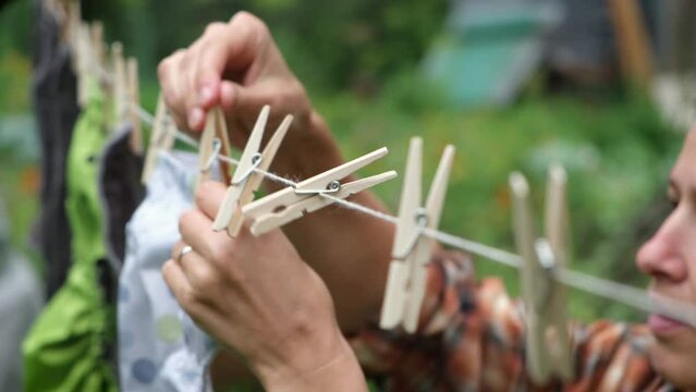 Close up woman hanging to clothspin reusable diapers to dry on clothesline in garden. Modern eco friendly cloth nappy for infant child hygiene. Sustainable lifestyle, zero waste concept.