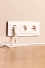 Group of white european electrical outlets with plug inserted into it on modern beige wall