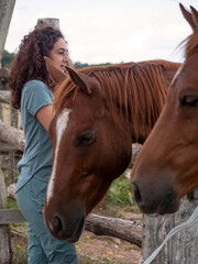 Vertical view of chetnut Angloarab horse looking at camera and Brunette woman looking melancholic at the horizon behinh some wooden post fence.  