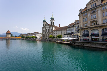 LUCERNE, SWITZERLAND, JUNE 21, 2022 - View of the Jesuit church of St. Franz Xaver and the Kapellbrücke Bridge on the background on the Reuss river in Lucerne, Switzerland