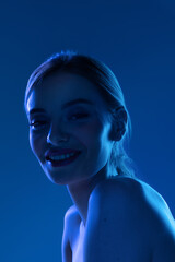 Portrait of female fashion model in neon light on blue gradient studio background. Beautiful caucasian girl with trendy make-up and well-kept skin.