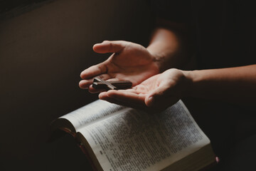 The cross rested on hand of young man while reading and studying bible, concept of faith for god.