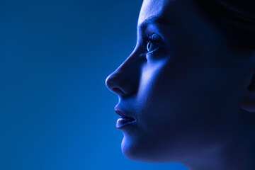 Closeup profile view of young pretty girl with well-kept skin isolated over dark blue background in neon light. Concept of art, fashion, style, inspiration