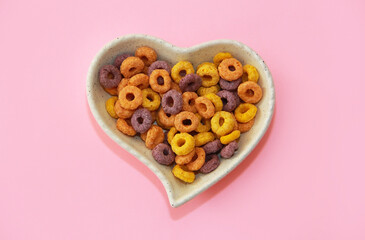 dry children's breakfast multicolored rings in a ceramic decorative plate in the form of a heart on a pink background