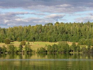 Autumn landscape in the Republic of Karelia, northwest Russia. Lake in calm weather, forest, haystacks on the field