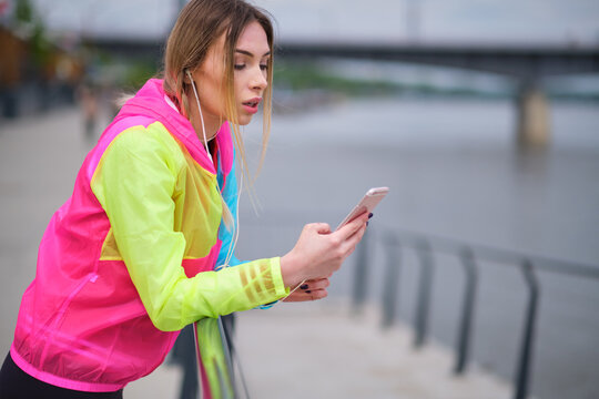 Fitness runner on mobile smart phone app tracking progress listening to music with earphones for fitness motivation. runner in sportswear relaxing sitting getting inspired.