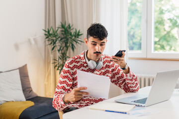 male student talking on mobile phone in his room, while doing homework