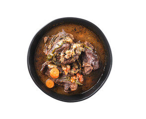 Traditional German braised beef cheeks in brown red wine sauce with herbs as closeup in black plate, top view, isolated on white