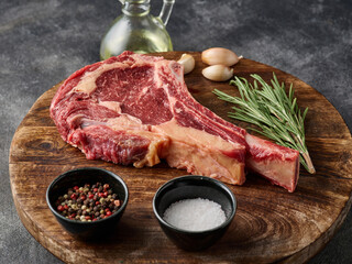 Raw tomahawk beef steak with ingredients for grilling, rosemary, salt, pepper and garlic. Close up.
