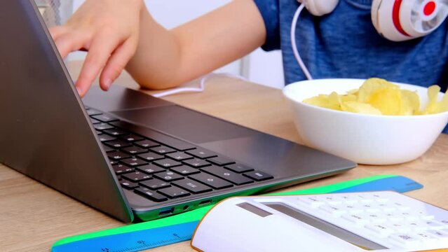 child, boy 8-9 years, primary school student sitting at laptop eating potato chips, browsing educational, developing materials on Internet, Back to school concept, doing homework, young businessman