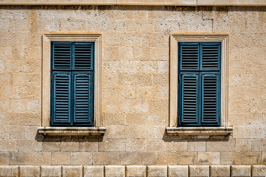 Two windows in old wall with closed shutters