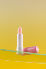  Moisturizing pink hygienic lipstick on a glass shelf on a yellow background.