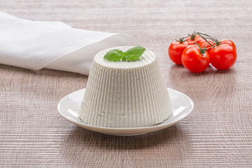 whole cottage cheese on white plate with basil leaf and tomatoes on wooden background