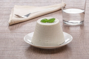 whole cottage cheese on white plate with basil leaf with glass of water on wooden background