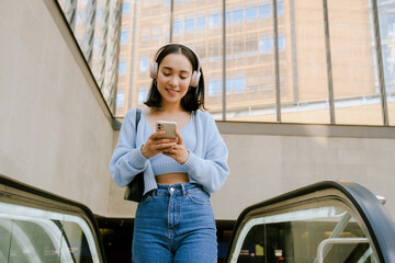 Young asian woman using mobile phone while standing on escalator