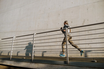 Asian woman running by concrete wall during workout outdoors