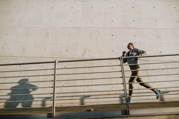 Asian woman running by concrete wall during workout outdoors