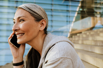 Asian mature woman talking on cellphone and sitting on stairs outdoors