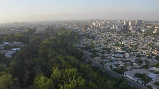View from the height of the roadway, cars, roofs of houses, parks. Panorama of an Asian city at sunset. Flight over the city of Osh, Kyrgyzstan.