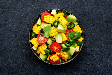 Tex-mex spicy salad with corn, avocado, jalapeno peppers, cherry tomatoes and cilantro. Black stone kitchen table background, top view, copy space