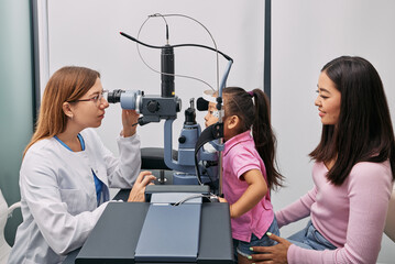 Japanese mother with her daughter while visit to optometrist. Little female child getting vision...