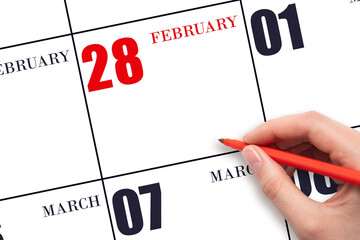 A hand holding a red pen and pointing on the calendar date February 28. Red calendar date, copy...
