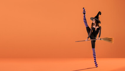 A ballerina on pointe shoes in a black witch costume in a hat and with a broom dances on an orange...