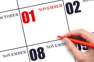 A hand holding a red pen and pointing on the calendar date November 1. Red calendar date, copy...