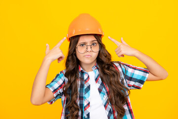 Funny face. Child builder in helmet. Teenage girl painter with painting brush tool or paint roller. Child on repairing work isolated on yellow background. Kids renovation concept.