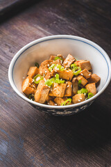 Stir fried tofu in a bowl with sesame seeds and herbs. Homemade healthy vegetarian Asian dish - fried tofu