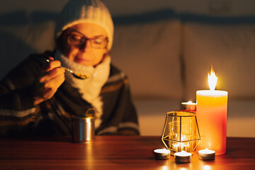 Woman eating canned food by candlelight. Electricity and gas outages in winter. Power cut.