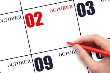 A hand holding a red pen and pointing on the calendar date October 2. Red calendar date, copy...