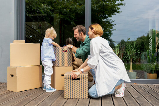 Joyful family unpacking moving boxes in front of their new home