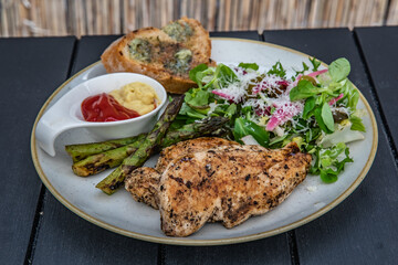 Grilled chicken fillet with asparagus, mustard, ketchup, salad and toast