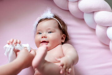 Hygiene - young mom wiping the baby skin body and face with wet wipes carefully on pink background....