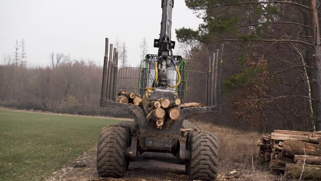 Grapple loader grappling and unloading logs on pile by forest road.