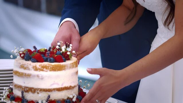 Hands of newlywed couple cutting fruit wedding cake together, close up.