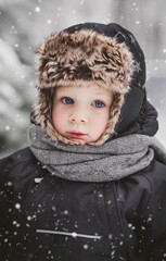 Portrait of a beautiful little European boy in winter under a snow-covered fir tree in the park. The concept of childhood and lifestyle.