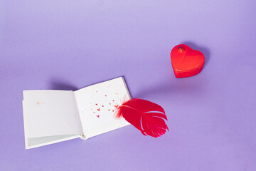 Red feather writing love letter on clear white paper decorated with hearts on purple background....