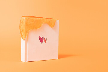 Two hearts on white book cover with glitter slime on vibrant orange color background with copy...