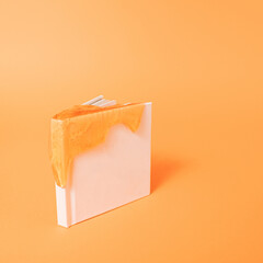 Empty white book cover with glitter slime on vibrant orange color background with copy space....