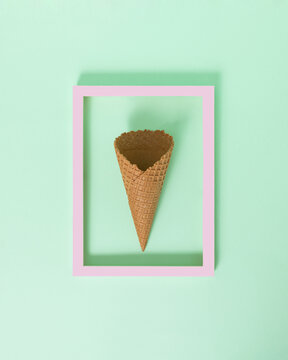 Empty ice cream cone in the purple frame on the pastel green background. Minimal sweet summer concept. Tasty tropical flat lay idea. Summer in the picture frame.