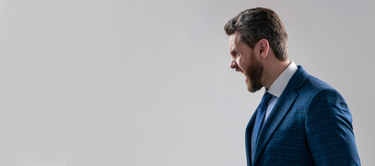 Man face portrait, banner with copy space. Business man in suit, isolated studio background, banner poster. You make me yell. Angry guy side-face yell grey background. Businessman scream. © Olena