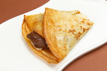 Pancakes with chocolate paste and banana in a plate.