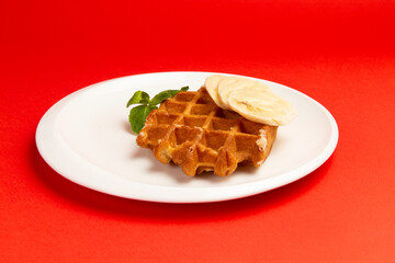 Waffles with banana in a plate on a red background.