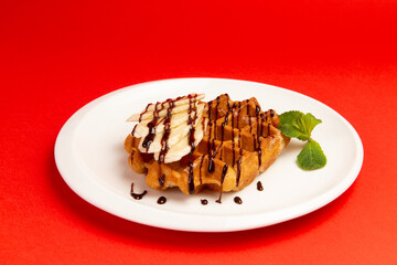 Waffles with banana in a plate on a red background.